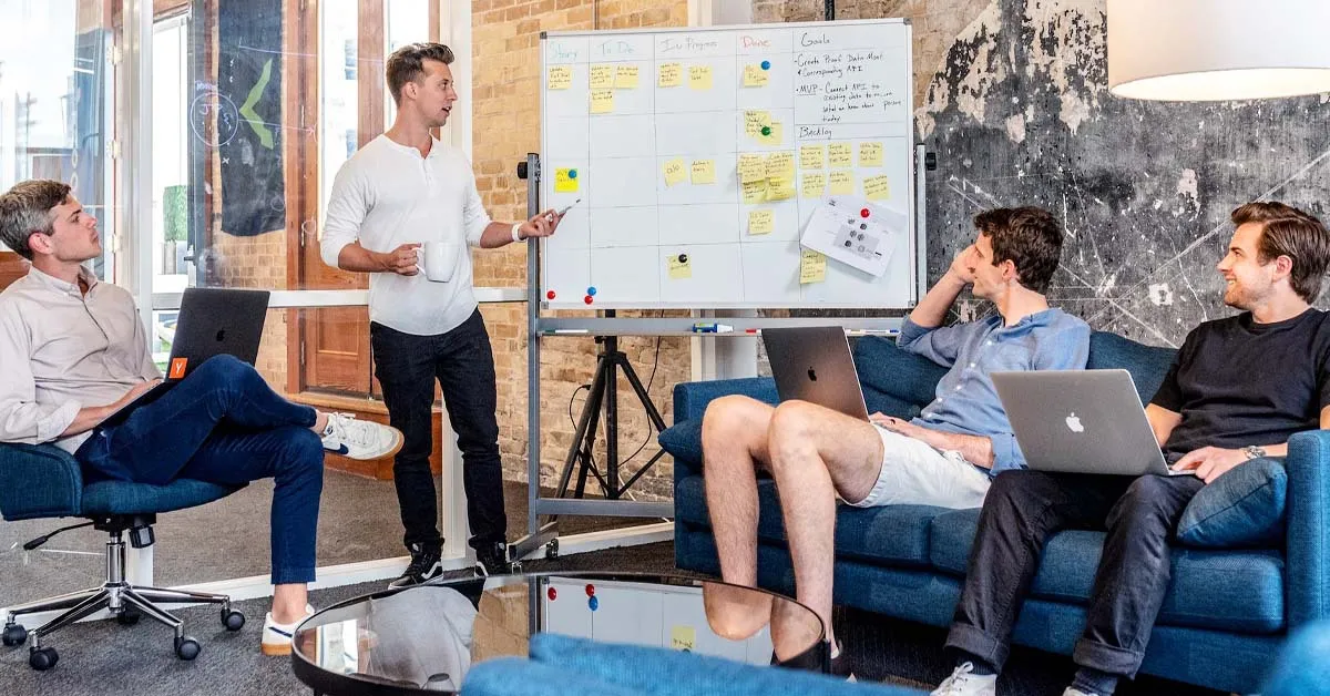 There are 4 men in the room for brainstorming. One of them is presenting some information, while 3 of them are seated. This image refers to an SEO agency.